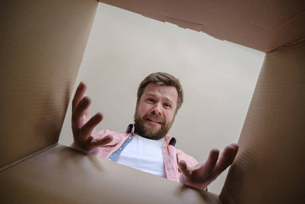 Very upset man found the wrong order in an unpacked delivered box, he cries and makes a gesture with hands. Unboxing inside view. - Photo, Image
