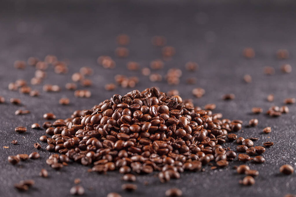 Freshly roasted aromatic coffee beans lie on a dark surface. Fresh morning fragrant drink concept - Fotó, kép