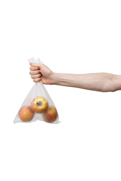 bolsa de polietileno en mano aislada sobre fondo blanco. hombre sosteniendo un paquete de manzanas amarillas frescas, rojas. parto durante la cuarentena de la pandemia de coronavirus COVID-19. suministros de alimentos, donación, voluntariado
 - Foto, imagen