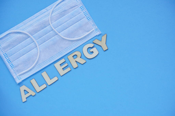 Слово "аллергия" сделано из деревянных букв и медицинской маски на синем фоне. Плоское представление о болезни аллергии
. - Фото, изображение
