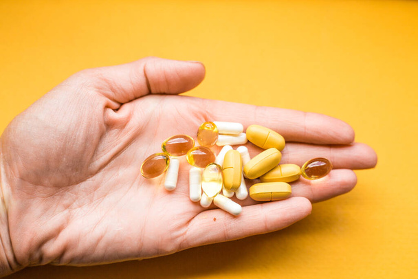 mão humana com comprimidos no fundo amarelo. contraste cores composição de cuidados de saúde
 - Foto, Imagem