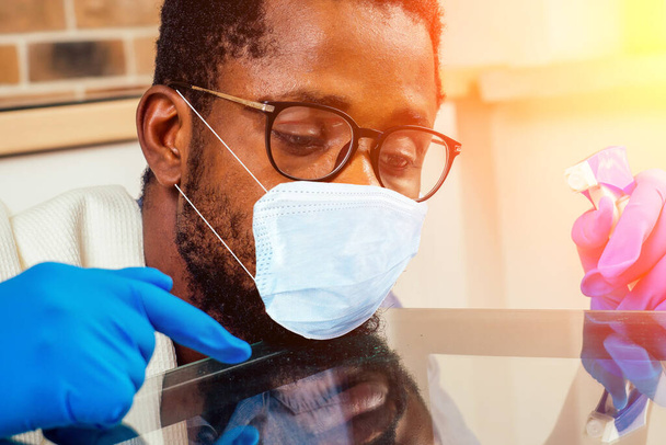 africký člověk v lékařské masce čištění vařič digestoř doma, cihlová zeď pozadí - Fotografie, Obrázek