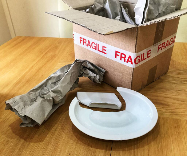 Відкрита картонна коробка з написом "Fragile" з паперовим пакунком та розбитою чашечкою. - Фото, зображення