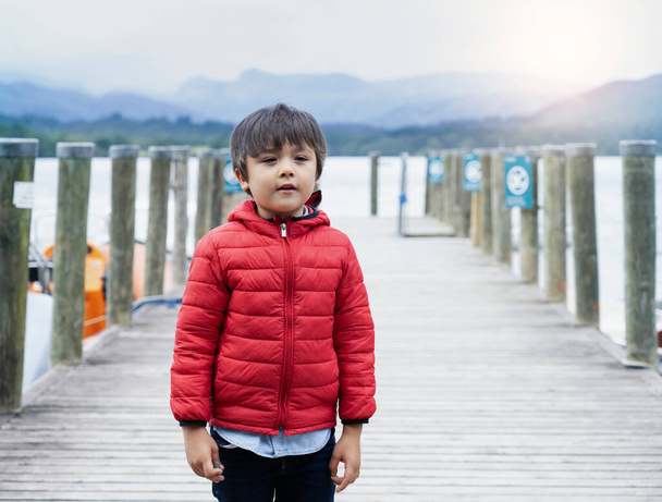 Candid portrait of adorable kid smiling face standing at pier by the lake, Hight key light shot mixed race child relaxing outdoor with blurry pier background - Photo, Image