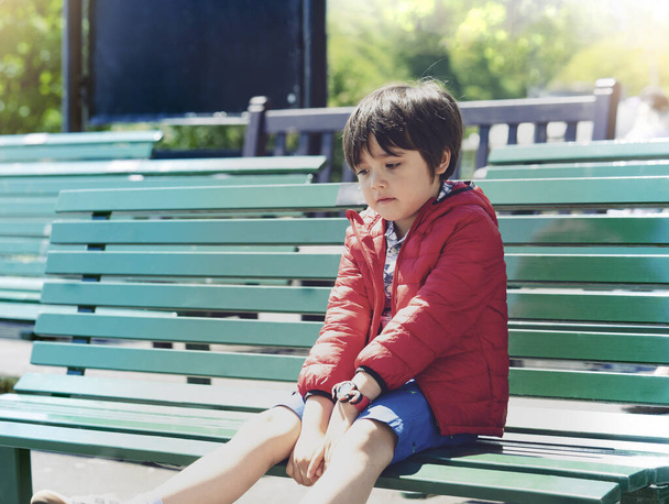 Zewnętrzny portret Smutnego Dzieciaka siedzącego samotnie metalowy płot, Emocjonalny portret zdenerwowanego chłopca patrzącego w dół z myślącą twarzą, Samotne dziecko z znudzoną twarzą, Rozpieszczona koncepcja dzieci - Zdjęcie, obraz