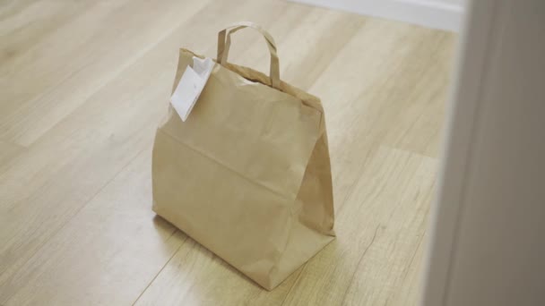 Dostawa żywności torba papierowa siedzi na zewnątrz drzwi - ręka z rękawicą lateksową podnosi go - Materiał filmowy, wideo
