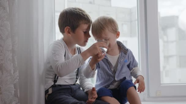 relationship of children, a caring older brother gives his little sib clear glass with cold pure water - Footage, Video