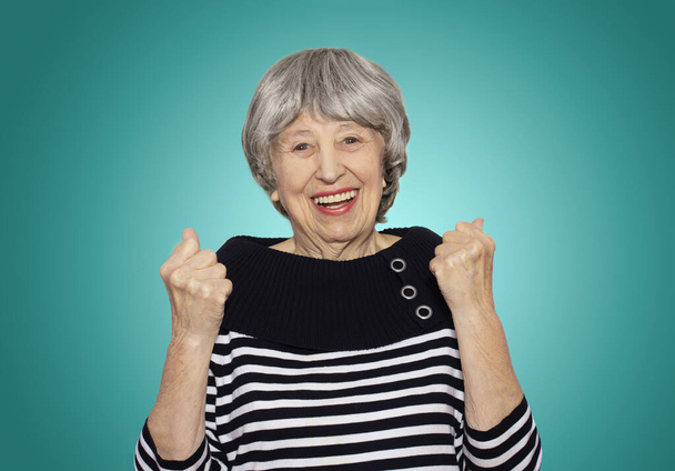 Het portret van een vrolijke glimlachende oudere vrouw gebaren overwinning op studio achtergrond - Foto, afbeelding
