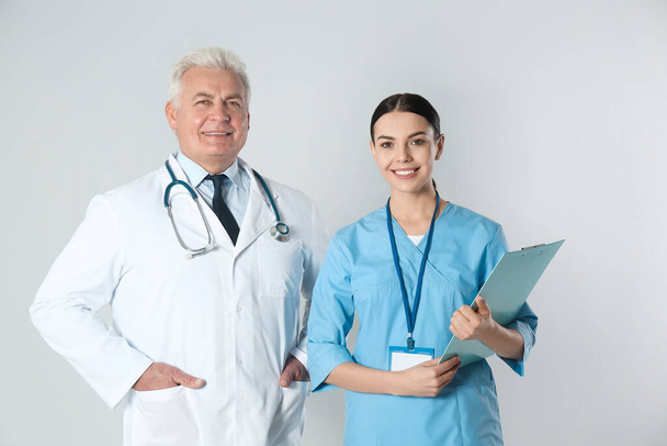 Senior doctor and young nurse against light background - Photo, image