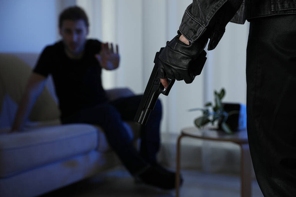 Man with gun and his victim in dark room, closeup. Dangerous criminal - Фото, зображення