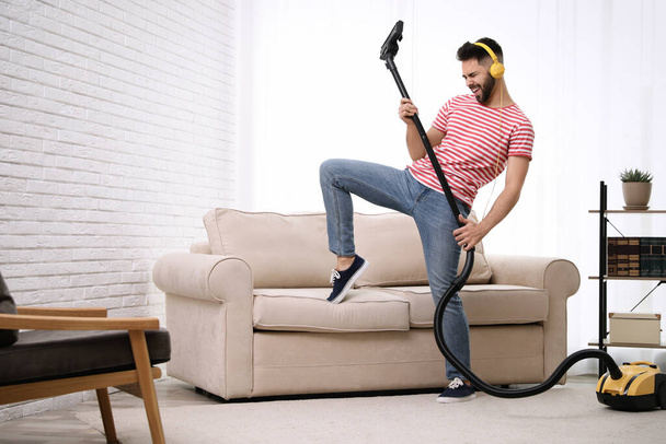 Young man having fun while vacuuming at home - Foto, Imagen