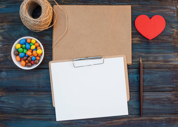 Изображение пустых конвертов и листа для каллиграфии, веревки, сладкого, чернильной ручки, красного сердца на деревянном фоне
 - Фото, изображение
