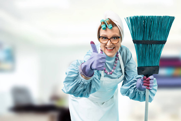 Elinde temizlik süpürgesi olan bir temizlikçinin portresi. Üniformalı bir temizlikçi kadın parlak bir ofise karşı duruyor. - Fotoğraf, Görsel