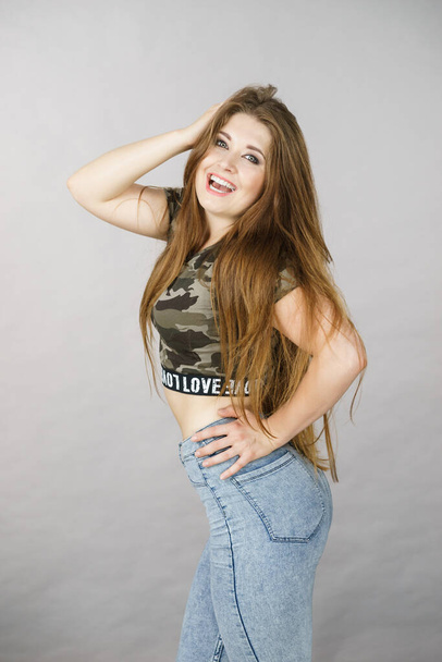 Feminine beauty concept. Portrait of beautiful young woman with long brown hair wearing stylish camo pattern tshirt and jeans - Фото, изображение