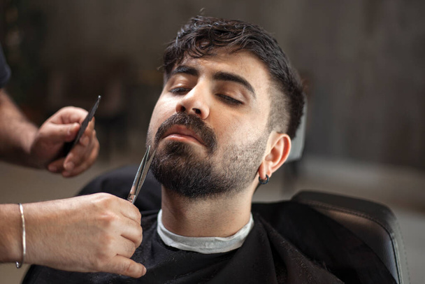  Männlicher Friseur bedient Klient, macht Haarschnitt mit Maschine und Kamm. - Foto, Bild