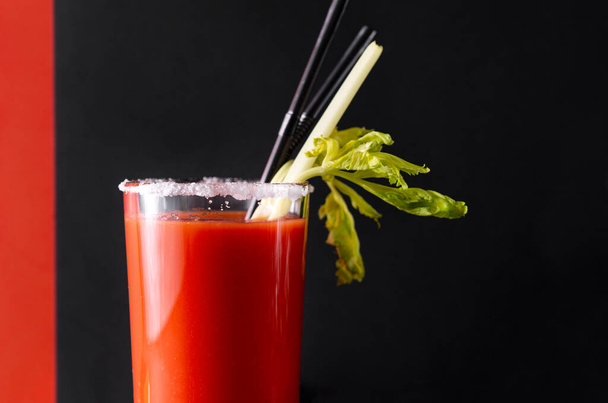 cocktail  bloody Mary , 1 glass of tomato juice with spices , salt ,  celery,  tubes  on a black and red background - Fotografie, Obrázek