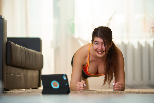Vrouwen in atletische workout kleding is het doen van een plank oefening tijdens het gebruik van video tutorials. - Foto, afbeelding
