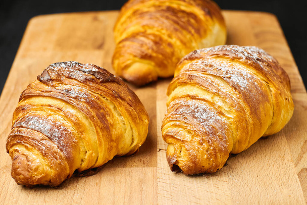 Feche três croissants recém-assados com açúcar em pó em uma mesa de madeira. Pastelaria francesa folhada
.  - Foto, Imagem
