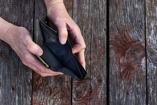 symbol ubóstwa i kryzysu finansowego, dwie zniedołężniałe ręce trzymają pusty portfel na drewnianym tle - Zdjęcie, obraz