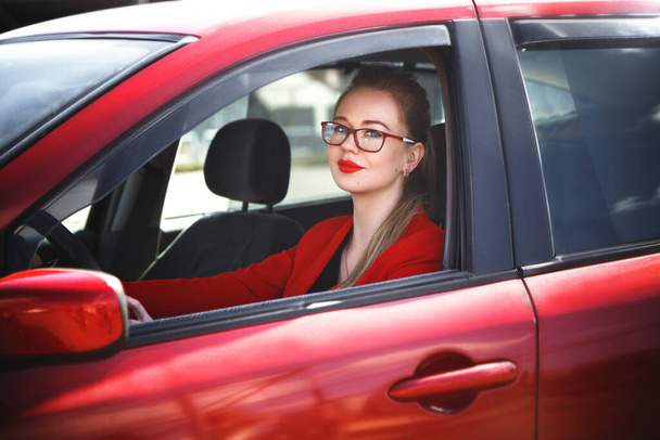 Young beautiful happy woman in red sitting at the wheel new training car. - 写真・画像