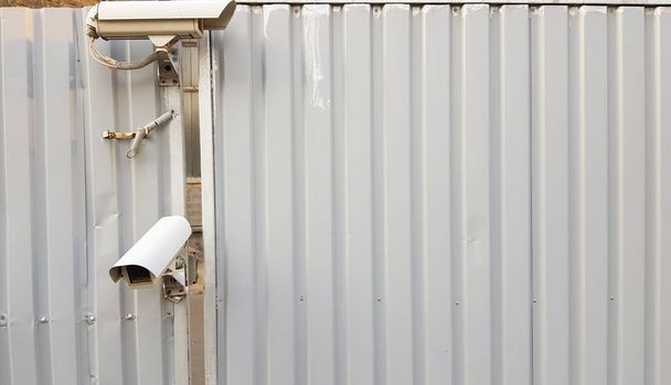 Surveillance camera on top of a gray corrugated metal fence. - Photo, Image