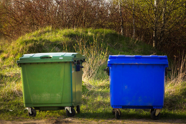 Dwa plastikowe pojemniki na śmieci stoją w wiosce na tle natury. jeden zielony, jeden niebieski - Zdjęcie, obraz
