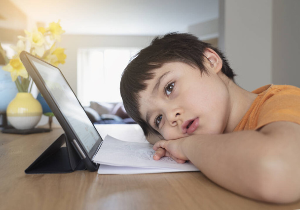 Dzieciak w izolacji za pomocą tabletu do pracy domowej, smutna twarz dziecka leżącego głową w dół patrząc w głąb myśli, chłopiec pobyt w domu podczas covid-19 zamknięcie - Zdjęcie, obraz