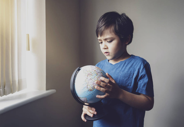 Self isolation Kid looking at globe learning about virus spreading around the world, Child boy with curious face finding the country have been lock down, Concept of COVID-19 pandemic infection. - Photo, Image