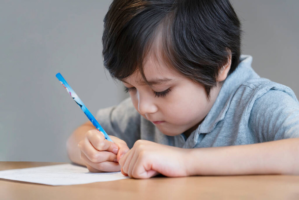 Portré iskolás fiú ül az asztalon csinál házi feladatot, Boldog gyermek kezében ceruza írás, Egy fiú rajz fehér papírt az asztalnál, Általános iskola és magániskola koncepció - Fotó, kép
