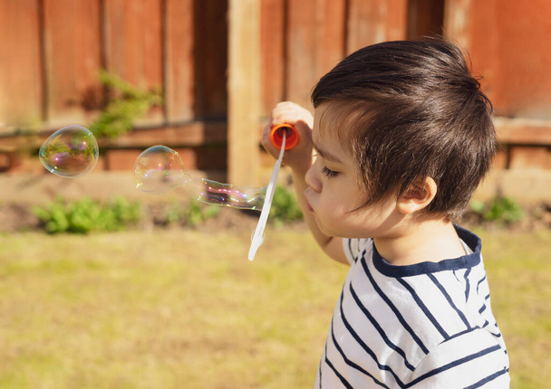Boldog fiú fúj szappanbuborékok a kertben, aranyos 4 éves gyerek fúj buborék pálca egy vicces arc, Aktív gyerek játszik a kertben egy napos nyári napon, Szabadtéri tevékenységek gyerekeknek - Fotó, kép