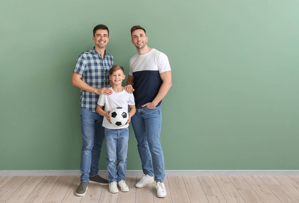 Happy gay couple and adopted child with soccer ball on color background - Photo, Image
