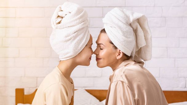 Mãe e sua filha adolescente vestindo toalhas de banho e abraços, tocando narizes dentro de casa, panorama
 - Foto, Imagem