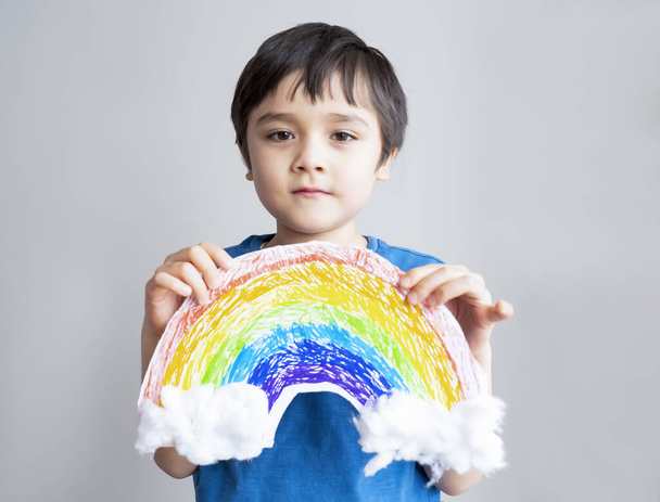 Ortrait  Kid inself isolation holding drawing picture of rainbow on white pape. Child Stay at home Social media campaign for coronavirus prevention concept - Photo, Image