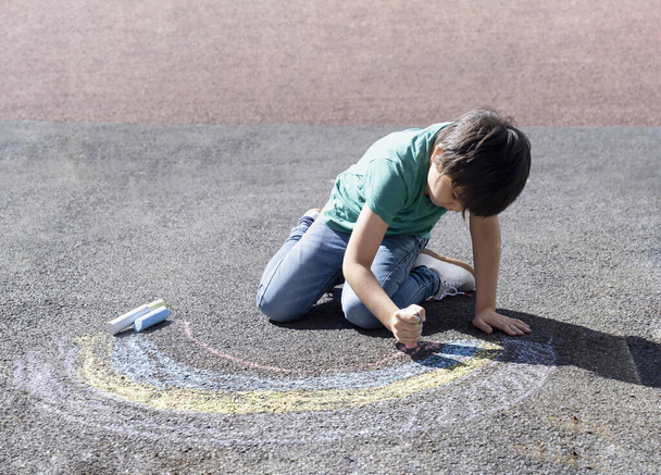 Ребенок раскрашивает радугу на тротуаре, ребенок рисует радугу с цветными мелом на тротуаре во время карантина Ковид-19 дома, домашнее обучение, кампания в социальных сетях по предотвращению коронавируса
 - Фото, изображение