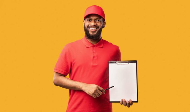 Delivery Man Holding Folder met blanco papier over gele achtergrond - Foto, afbeelding