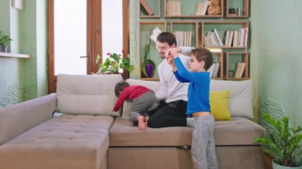 Щасливі і смішні двоє маленьких дітей грають зі своїм батьком на дивані у вітальні вони насолоджуються разом відчуттям щасливого і збудженого
 - Кадри, відео