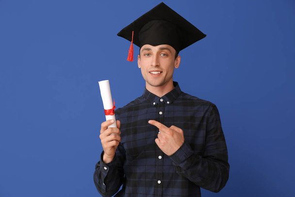 Młody człowiek w kapeluszu dyplomowym i z dyplomem na tle koloru - Zdjęcie, obraz