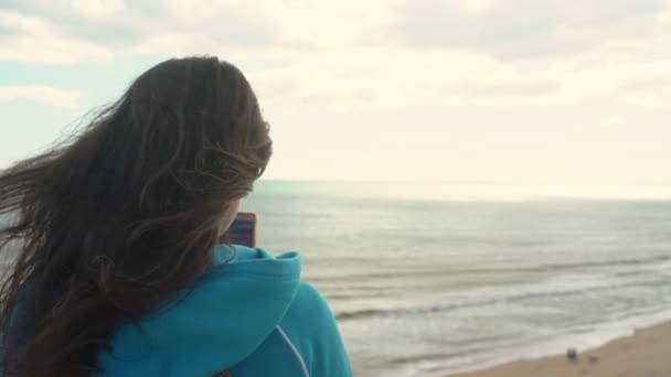 Mladá dívka turista na pláži u oceánu s telefonem v ruce bude fotit krajinu kolem něj. - Záběry, video