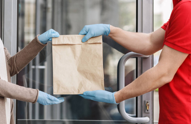 Corriere in guanti di gomma consegna sacchetto di carta al cliente a casa
. - Foto, immagini