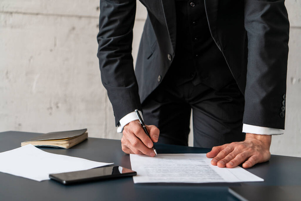 Standing businessman signing contract at table - Photo, Image