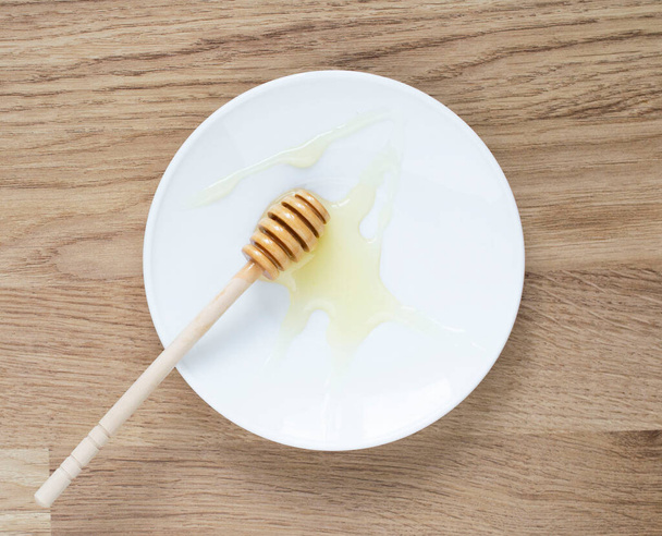 pau de madeira de mel em um pires branco. mel pingando de pau de mel
. - Foto, Imagem
