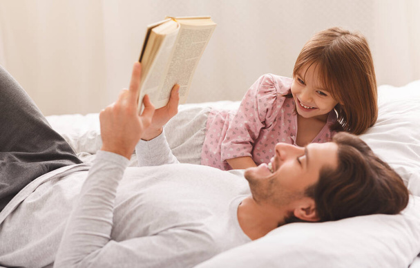 Young father reading book to little daughter, laying on bed - Fotoğraf, Görsel