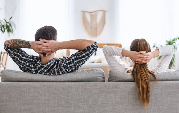 Repos commun. Guy et fille se détendre sur le canapé avec les mains serrées derrière la tête
. - Photo, image