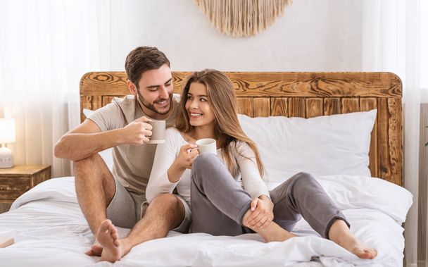 Szczęśliwa para w sypialni na łóżku i drinki z kubków - Zdjęcie, obraz