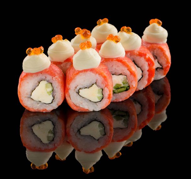 Uramaki Sushi roll with salmon, cheese, cucumber, sauce and caviar on top isolated on black background with reflection - Foto, afbeelding