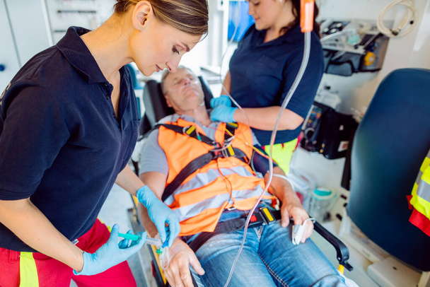 Spoedeisende arts die druppel injectie geeft aan gewonde man in ambulance - Foto, afbeelding
