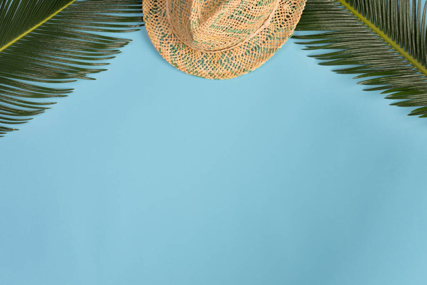 Summer composition. Tropical leaves and wtraw hat on blue background. Summer concept. Flat lay, top view, copy space - Photo, Image