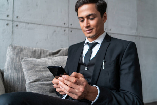 Friendly young businessman with phone in armchair - Foto, Bild