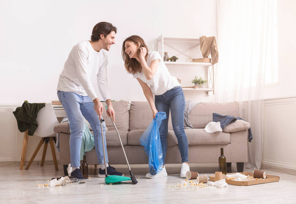 Rindo jovem casal limpeza bagunça em seu apartamento após a festa
 - Foto, Imagem