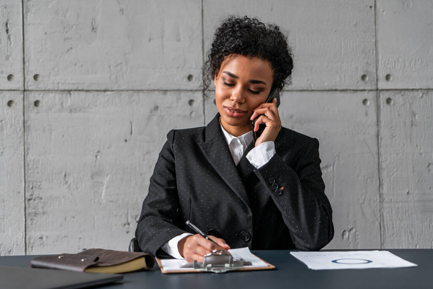 African businesswoman on phone taking notes - Foto, Bild